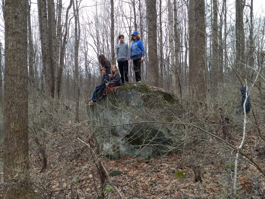 a group of 5 campers sit and stand on a large rock that  is taller than they are